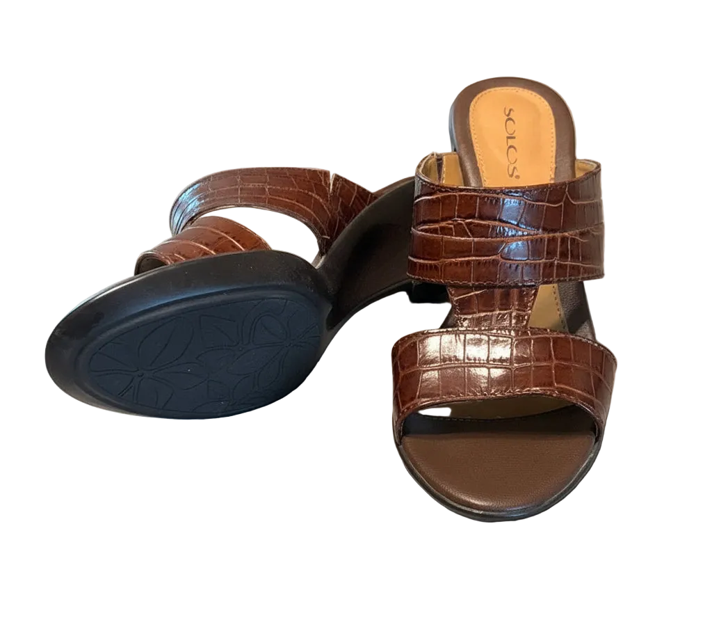 A pair of brown crocodile-embossed slide sandals with wedge heels.
